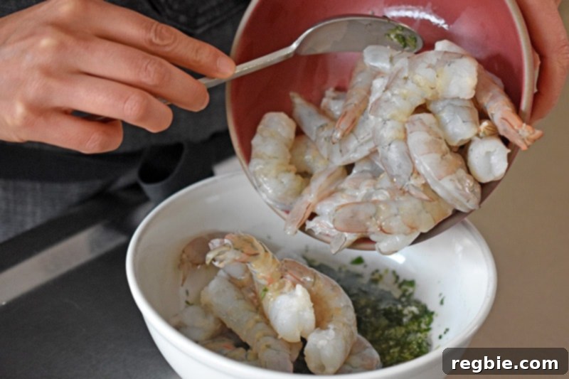 Someone is adding fresh, raw shrimp to a bowl of fragrant marinade, preparing them for delicious paleo, Whole30, and keto shrimp tacos.
