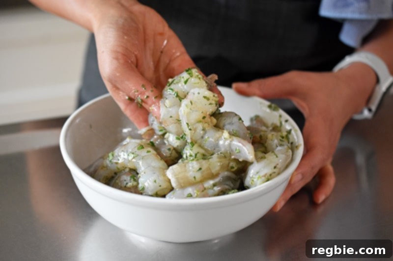 Someone is mixing by hand the shrimp in the bowl of marinade, ensuring even coating before refrigeration.
