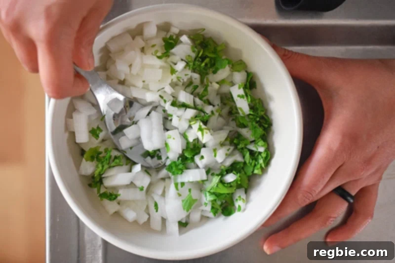 Someone stirring in a small bowl diced white onions with chopped cilantro, preparing a fresh topping for the tacos.