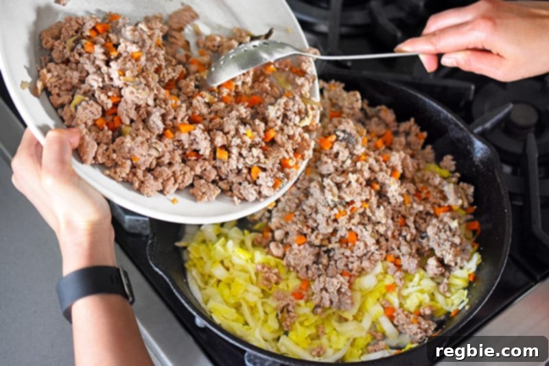 Returning the cooked ground pork to the skillet, mixing it with the wilted Napa cabbage for a cohesive Egg Roll in a Bowl.