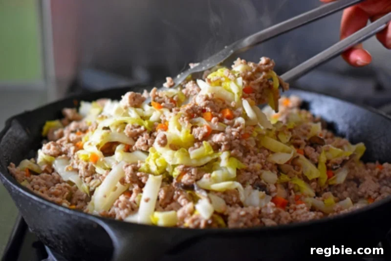 Tossing all the ingredients for Egg Roll in a Bowl in the skillet with metal tongs, ensuring everything is thoroughly mixed.