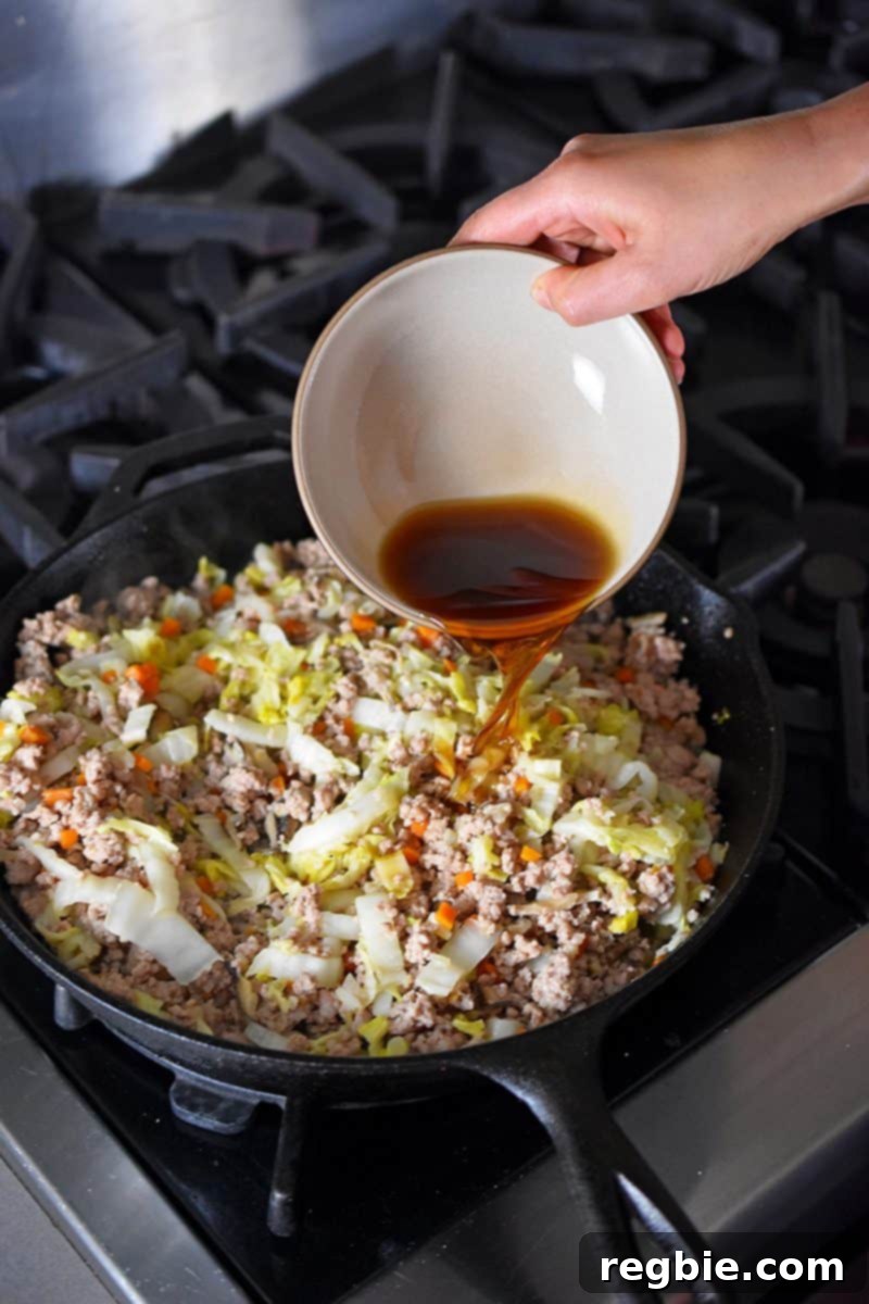 Pouring the savory seasoning sauce, including coconut aminos and fish sauce, into the skillet of Egg Roll in a Bowl.