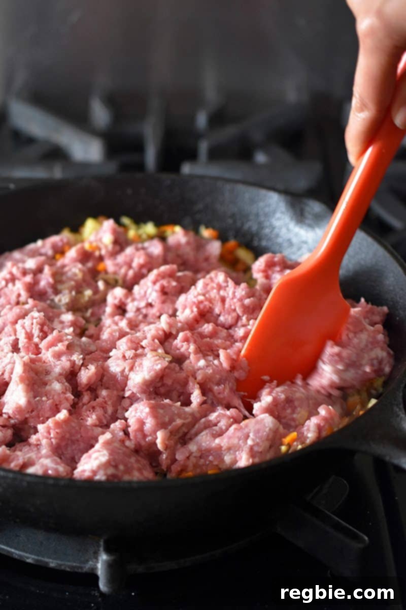 Stirring ground pork into the skillet with sautéed vegetables, breaking up the meat for even cooking in the Egg Roll in a Bowl.