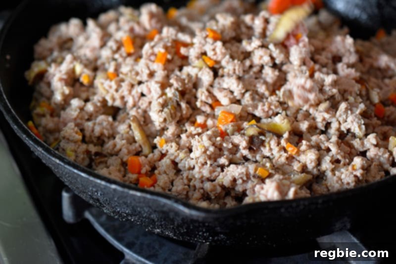A close-up shot of perfectly browned ground pork mixed with vegetables, nearing completion in the cast iron skillet.