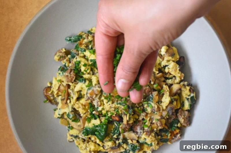 An overhead shot of a hand adding fresh, chopped chives as a vibrant garnish to the finished Joe’s Special Scramble.