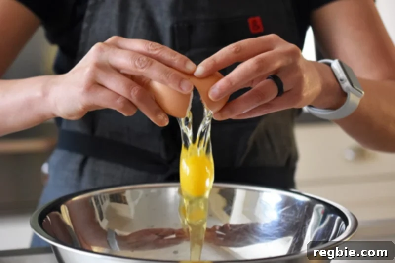 Cracking an egg into a large metal mixing bowl, preparing for the scramble.