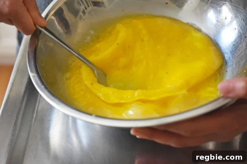 An overhead shot of someone whisking eggs in a metal bowl with a fork, ensuring a well-combined and airy mixture.