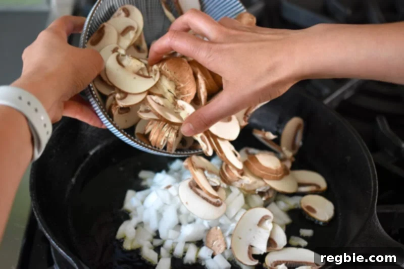 Adding diced onions and sliced mushrooms to a sizzling cast iron skillet, starting the sauté process.