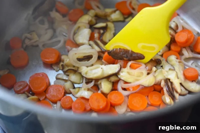 An overhead shot of the beautifully sautéed shallots, carrots, and shiitake mushrooms in the saucepan, ready for broth.