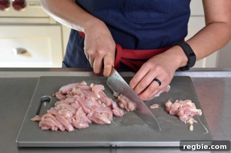 A person is expertly slicing boneless, skinless chicken thighs into thin strips, preparing them for the Watercress & Chicken Soup.