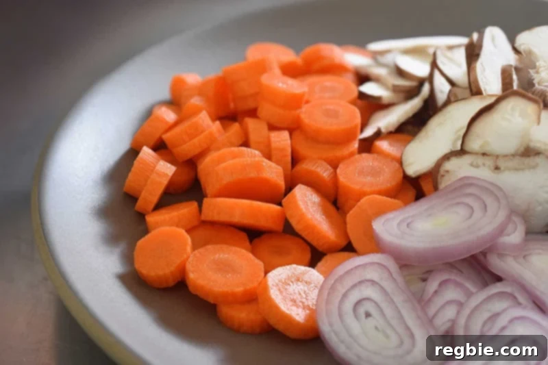 A colorful platter showcasing perfectly sliced carrot coins, shiitake mushrooms, and shallots, ready for the soup.