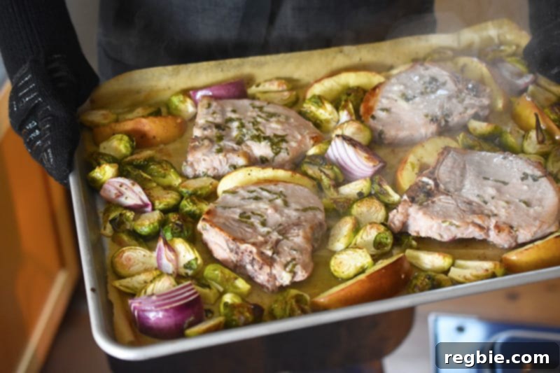 Removing Sheet Pan Pork Chop Supper from the oven, showing the browned pork and caramelized vegetables.