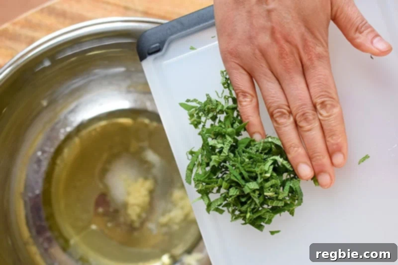 Adding the marinade ingredients for Sheet Pan Pork Chop Supper to a large metal mixing bowl, including olive oil, lemon juice, sage, garlic, and salt.