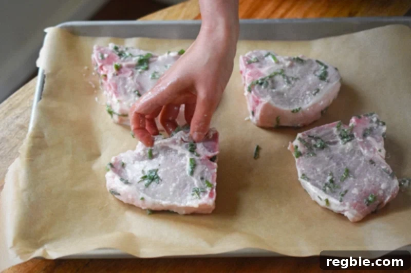 Placing pork chops in a single layer on a rimmed baking sheet, ready for roasting.