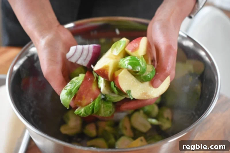Tossing the apples, onions, and Brussels sprouts in the marinade bowl, ensuring they are evenly coated.