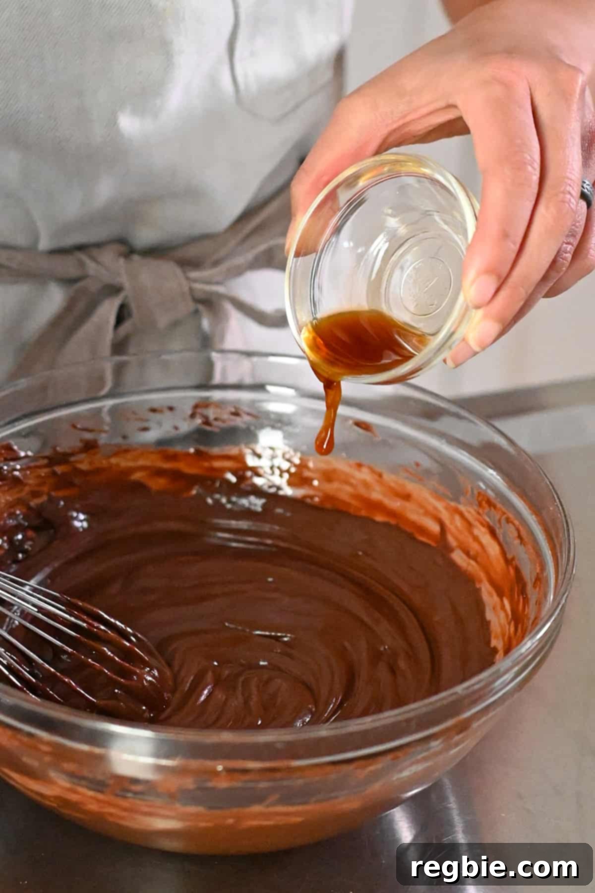 A closeup of pouring vanilla extract into a teaspoon, highlighting the addition of flavoring to the ganache.