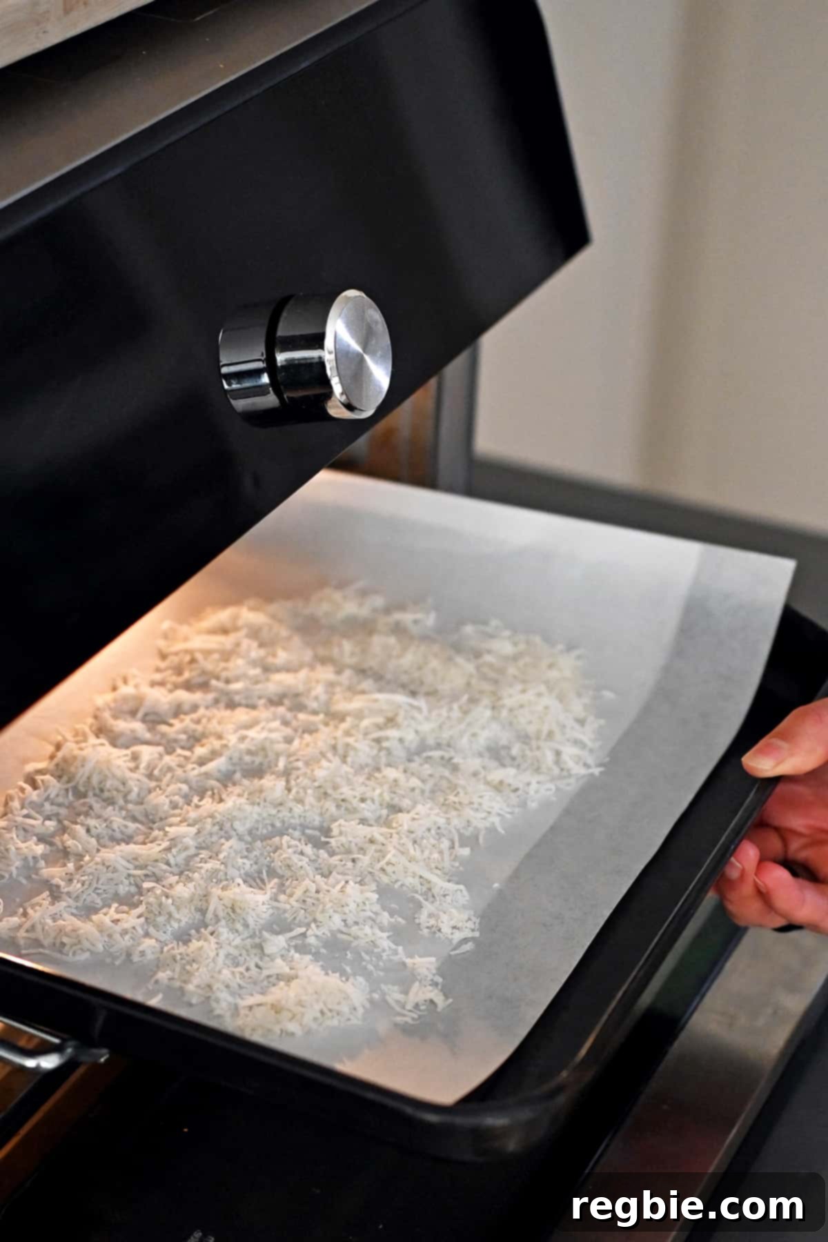 A rimmed baking sheet with a layer of shredded coconut is placed in a toaster oven, illustrating the toasting process for the truffle coating.