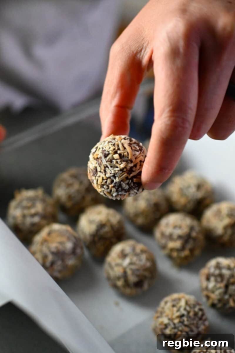 A hand is placing paleo truffles into a storage container lined with parchment paper, demonstrating proper storage technique.