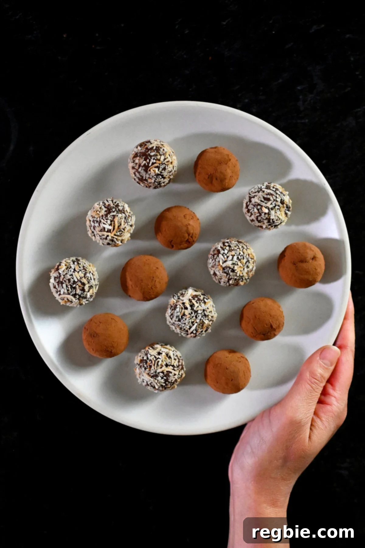 A closeup of two Nom Nom Paleo Chocolate Truffles covered with toasted shredded coconut, ready to be enjoyed.