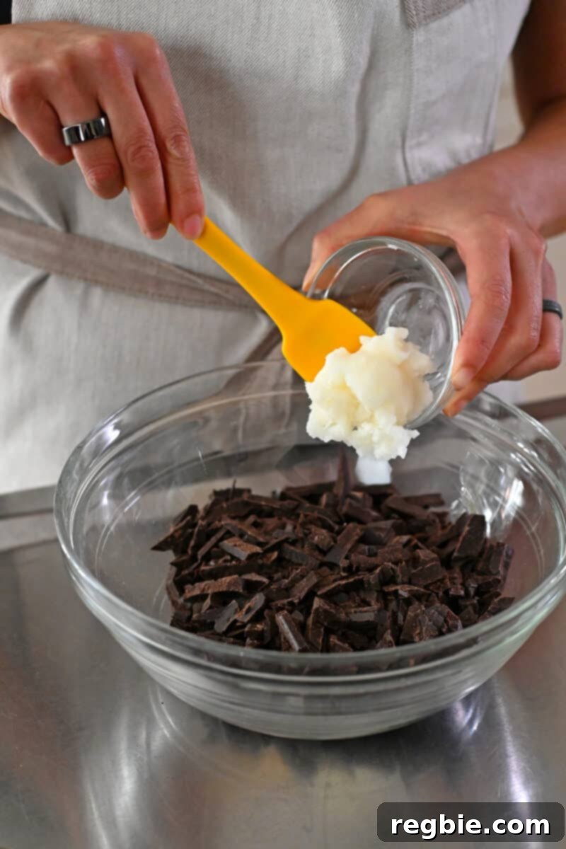 Adding refined coconut oil to a bowl filled with finely chopped dark chocolate, ready for the ganache making process.