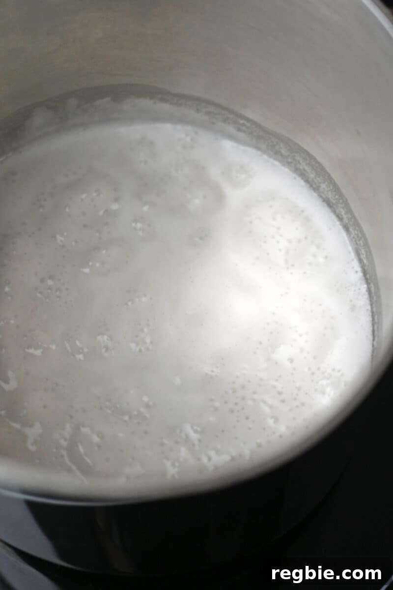 A closeup shot of simmering coconut milk in a saucepan, a crucial step for creating a smooth vegan ganache base.