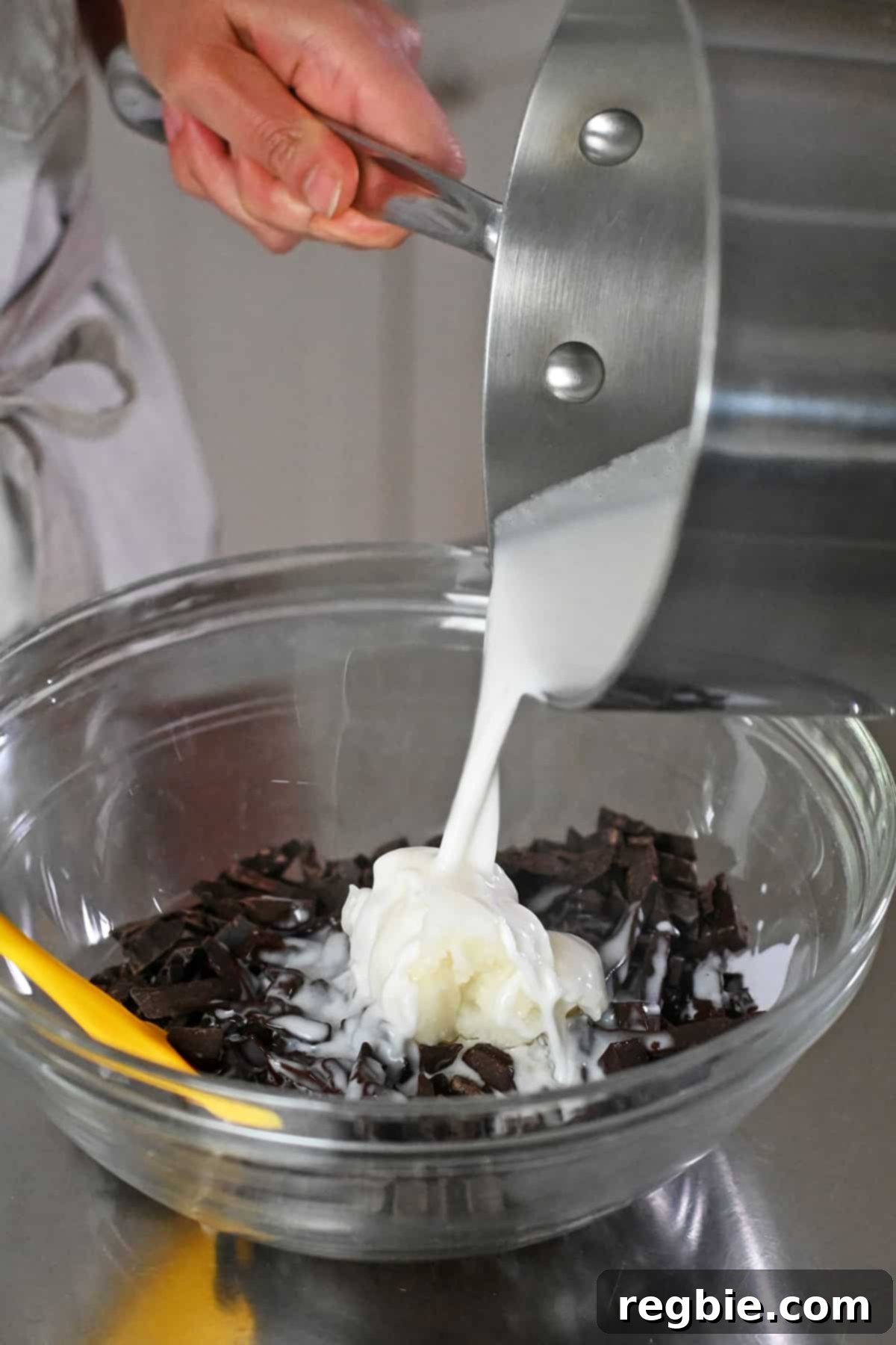 Pouring warm coconut milk into a bowl filled with dark chocolate slivers and coconut oil, initiating the ganache formation.