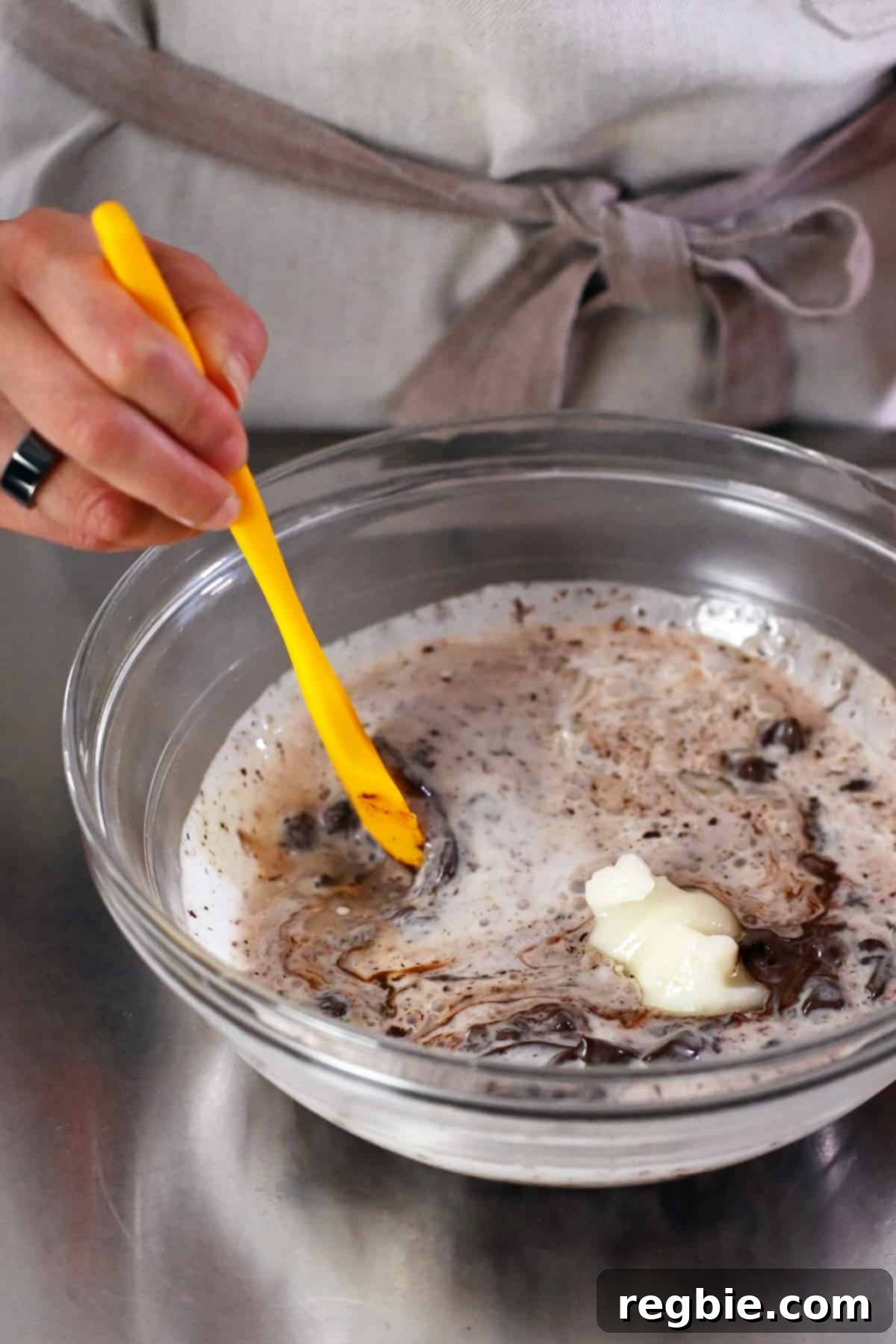 Closeup of stirring the Nom Nom Chocolate truffle base with a rubber spatula, showing the chocolate melting into the warm coconut mixture.