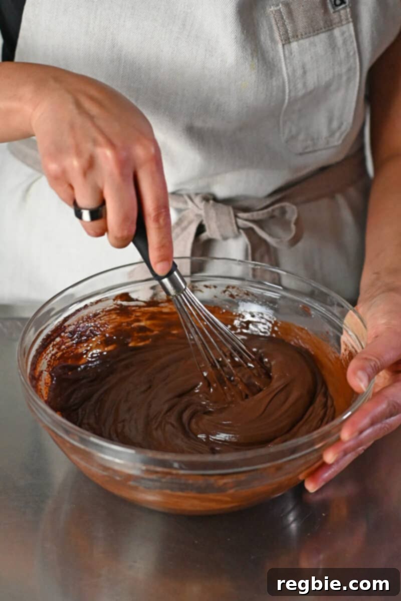 Whisking paleo and vegan chocolate ganache to make chocolate truffles in a clear glass bowl, illustrating the transformation into a smooth emulsion.