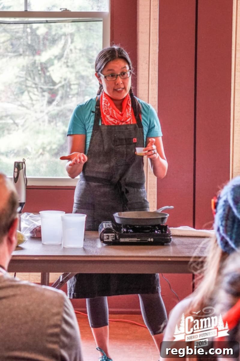 The Camp That Made Us Smarter and Stronger 2 Michelle Tam at Camp Nerd Fitness, leading a cooking demonstration. She's holding a pan and smiling, surrounded by an enthusiastic audience in a rustic camp setting.