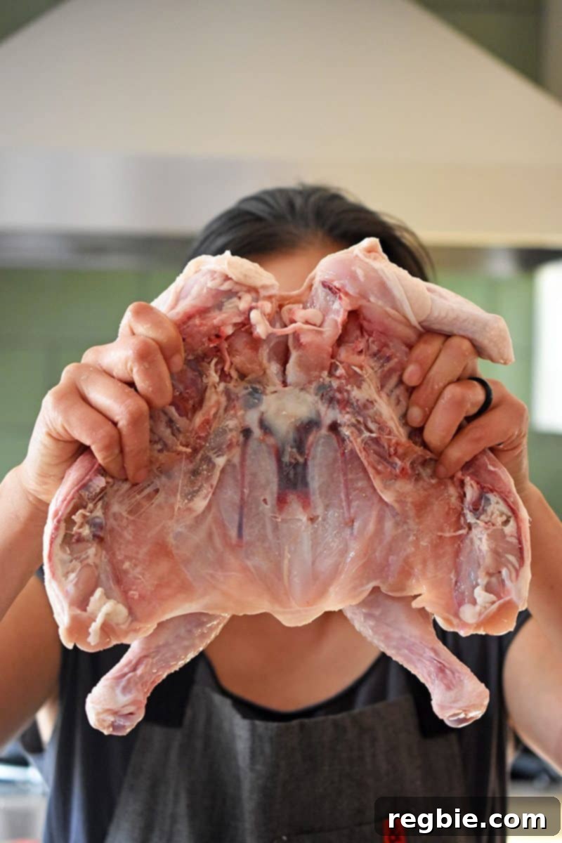 Transform Chicken with Herb Butter Spatchcock Juicy and Crispy 8 Holding a flattened chicken in front of a person's face, illustrating its 'facehugger' appearance.