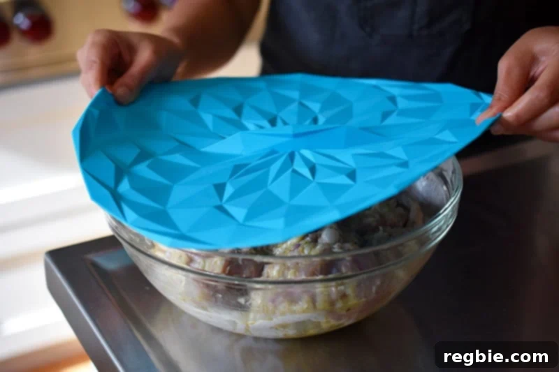 Covering a bowl of marinated Vietnamese Lemongrass Chicken with a silicone lid before refrigeration.