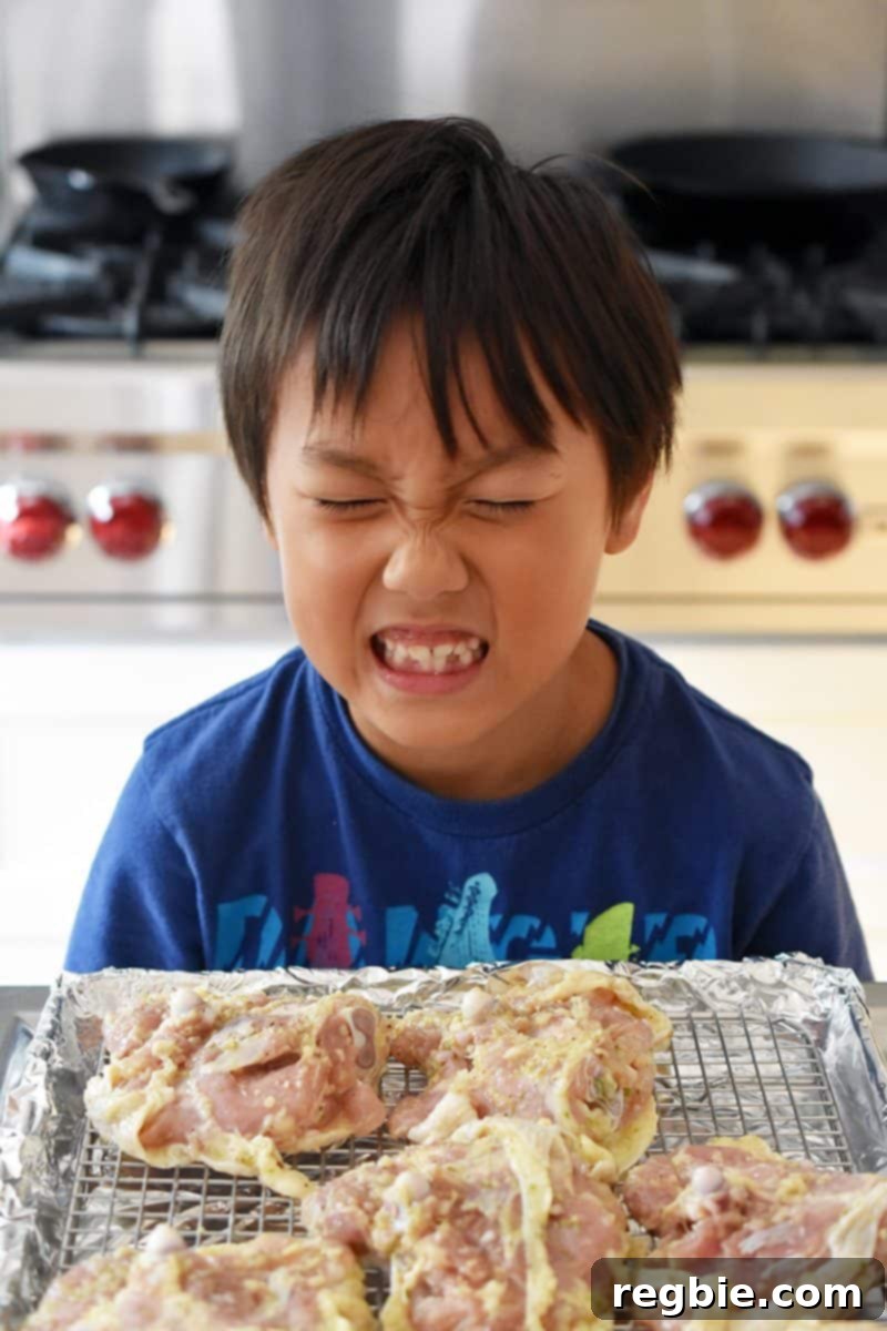A child making a funny face in front of a tray of raw Vietnamese Lemongrass Chicken, ready for the oven.
