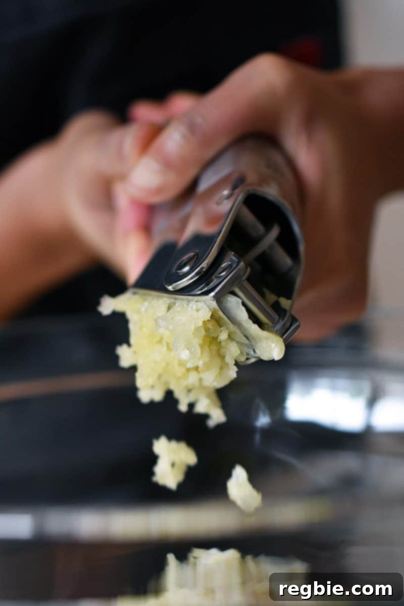 Adding minced garlic from a garlic press to the aromatic marinade for Vietnamese Lemongrass Chicken.