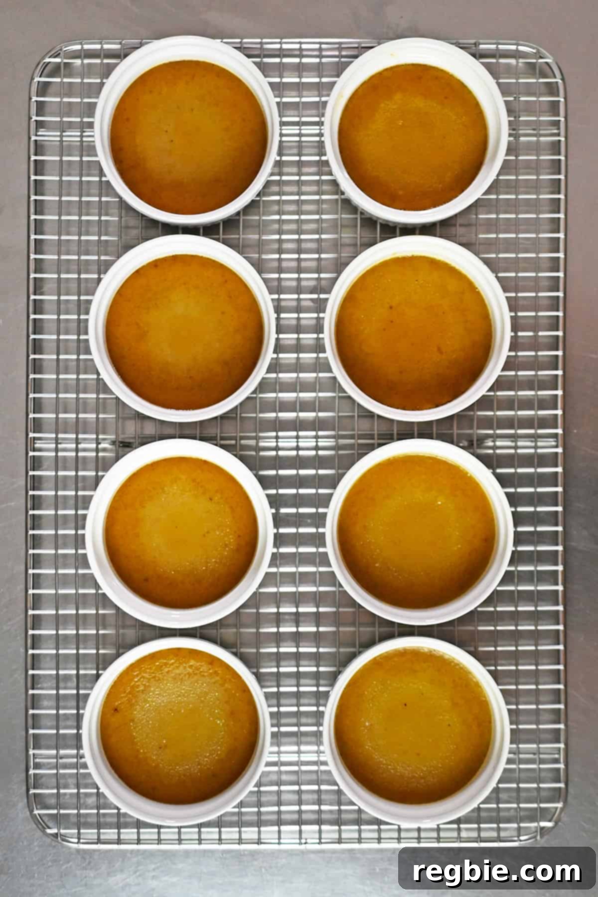 Decadent Paleo Pumpkin Custard 14 An overhead shot of freshly cooked pumpkin custards in white ramekins, cooling neatly on a wire rack.