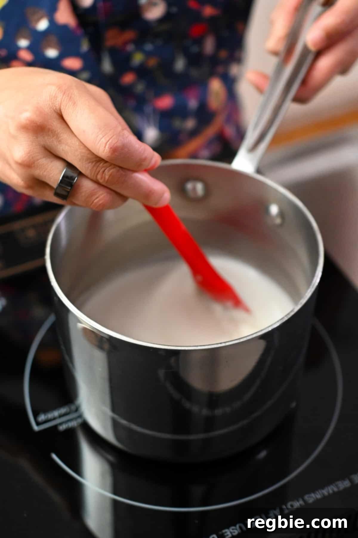 Decadent Paleo Pumpkin Custard 5 A red spatula is stirring coconut milk simmering in a small saucepan over a low flame, producing gentle steam.