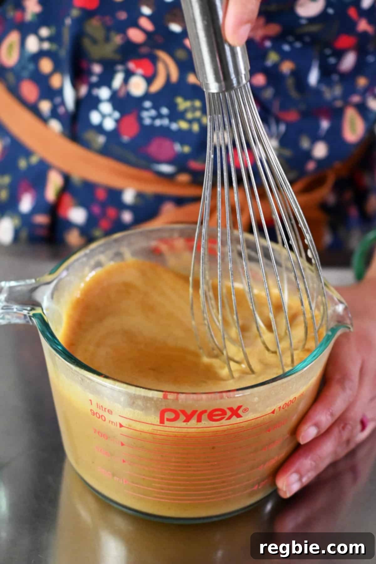 Decadent Paleo Pumpkin Custard 9 A hand is vigorously whisking the ingredients for pumpkin custard in a large measuring cup, ensuring everything is well combined.