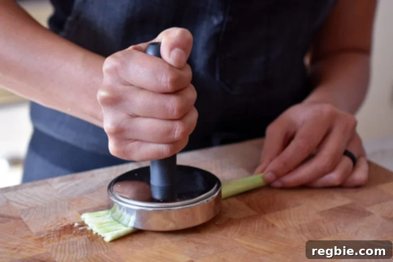 Lemongrass Cooking Guide 11 Smashing a piece of trimmed lemongrass with a metal meat pounder on a wooden cutting board.