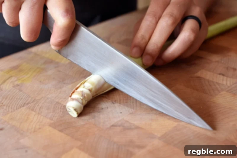 Lemongrass Cooking Guide 4 Cutting the tough end off of a lemongrass stalk on a wooden cutting board.