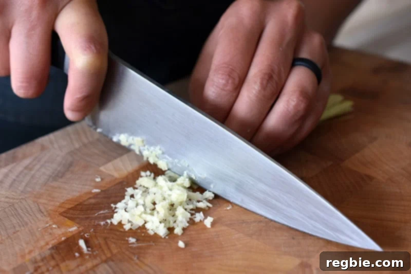 Lemongrass Cooking Guide 9 Mincing a trimmed and smashed piece of lemongrass with a chef's knife on a wooden cutting board.