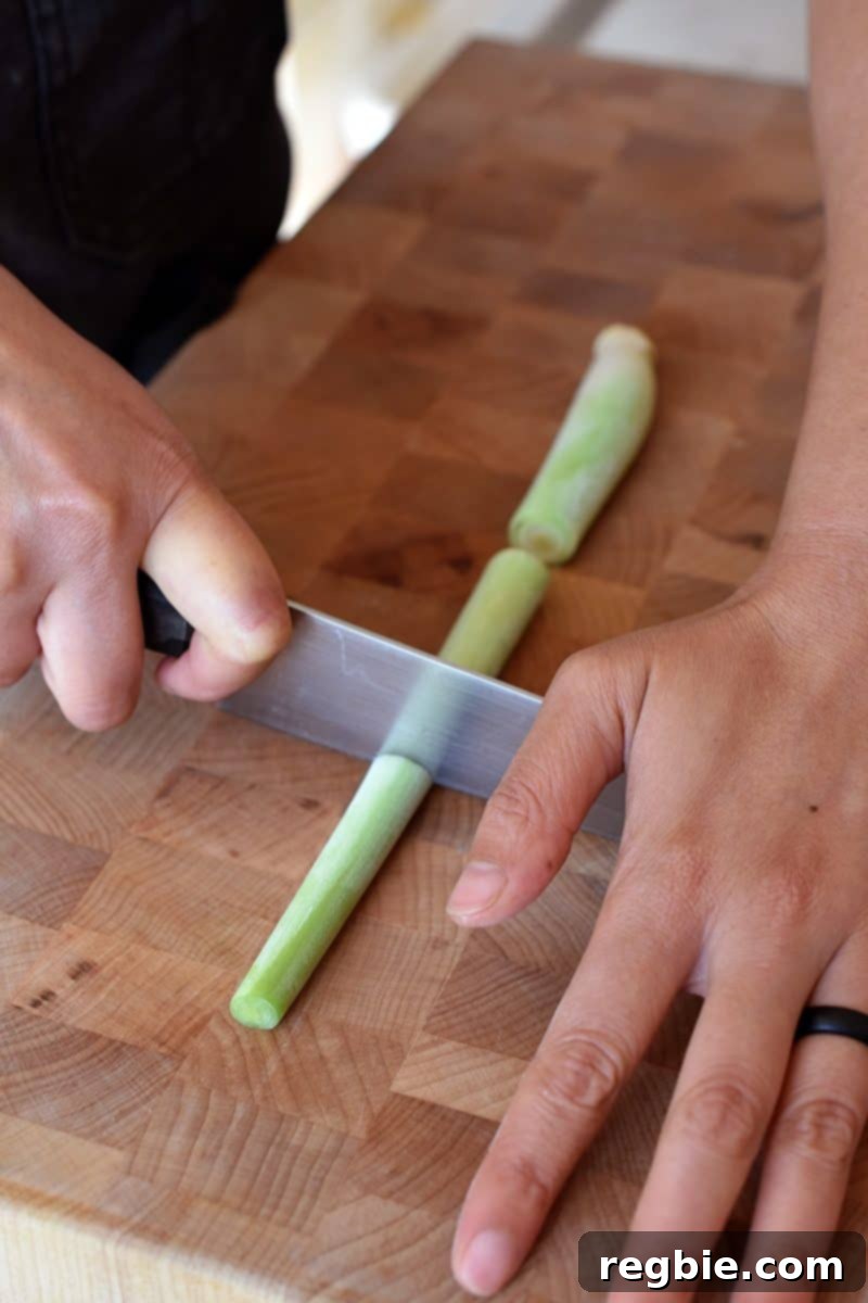 Lemongrass Cooking Guide 10 Cutting a trimmed piece of lemongrass into three pieces on a wooden cutting board.