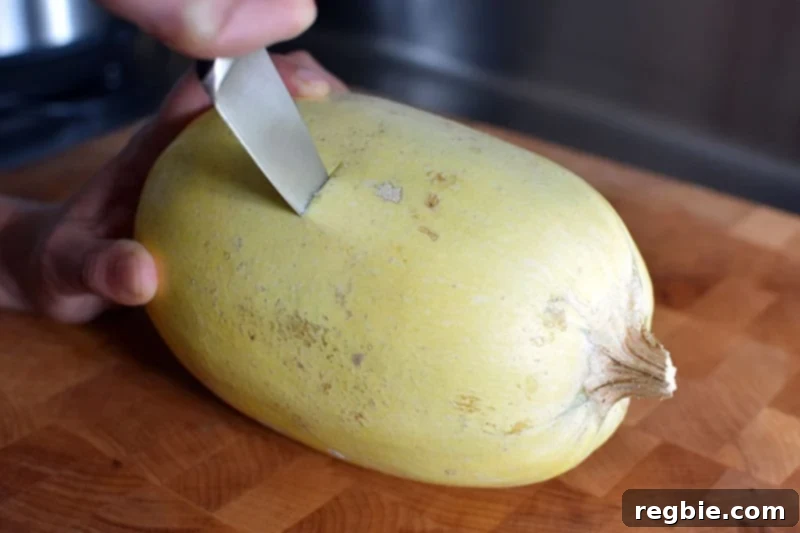 Quick Foolproof Instant Pot Spaghetti Squash 5 A small spaghetti squash resting on a cutting board, with a paring knife inserted crosswise through its middle, demonstrating the correct cutting technique for longer strands of squash.