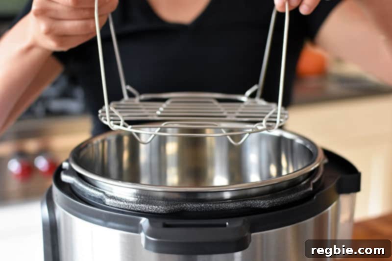 Quick Foolproof Instant Pot Spaghetti Squash 8 A close-up view of two hands carefully lowering a stainless steel steaming rack into the inner pot of an open Instant Pot, setting up for pressure cooking.