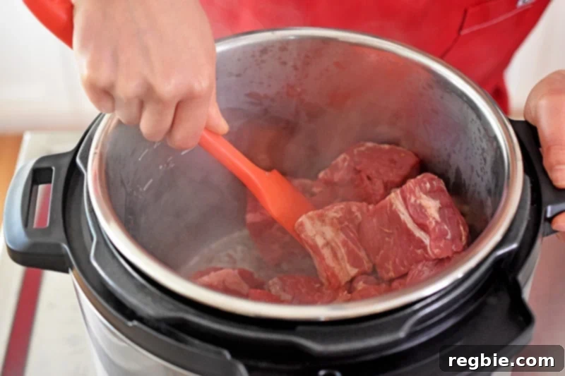 Browning the pork cubes on the sauté function in an open Instant Pot.