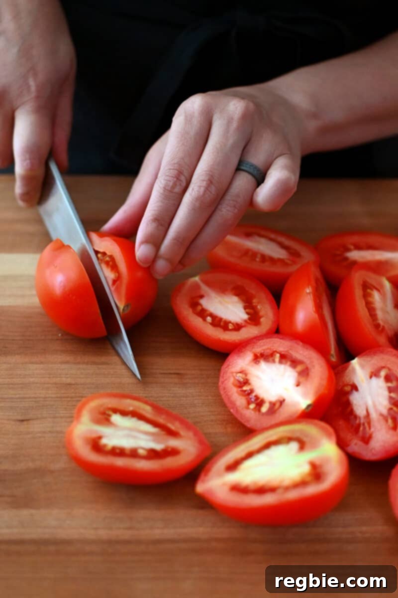 Umami-Packed Oven-Roasted Tomatoes: Easy, Whole30, Keto, Low Carb 5 Slicing roma tomatoes in half lengthwise on a wooden cutting board.