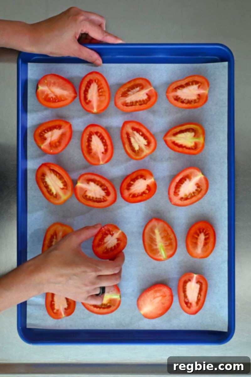 Umami-Packed Oven-Roasted Tomatoes: Easy, Whole30, Keto, Low Carb 6 An overhead shot of two hands arranging halved Roma tomatoes on a blue baking sheet.