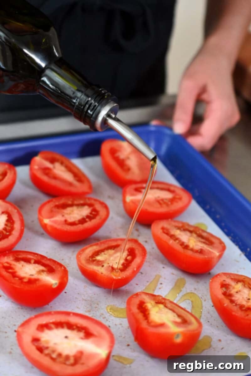 Umami-Packed Oven-Roasted Tomatoes: Easy, Whole30, Keto, Low Carb 8 Drizzling extra virgin olive oil on halved tomatoes on a blue baking sheet.
