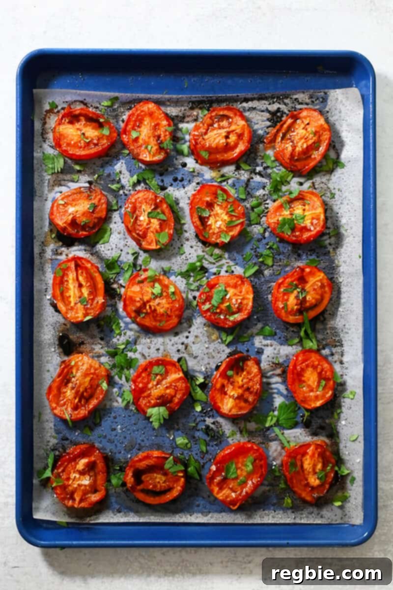 Umami-Packed Oven-Roasted Tomatoes: Easy, Whole30, Keto, Low Carb 10 An overhead shot of a blue baking sheet with oven roasted tomatoes drizzled with balsamic vinegar and fresh herbs.