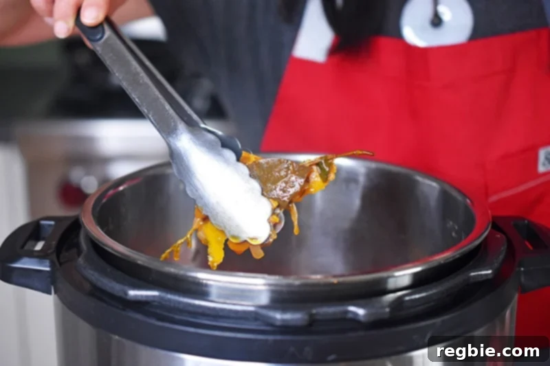 Removing the dried herbs and orange zest from the Instant Pot with a pair of tongs before blending the gravy.