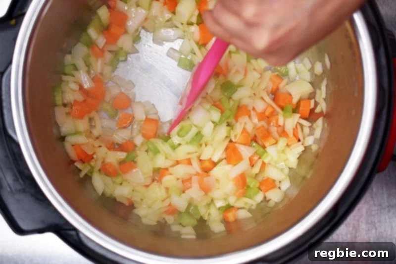 An overhead shot of an open Instant Pot with the mirepoix mixture sautéing for the base of the orange duck gravy.