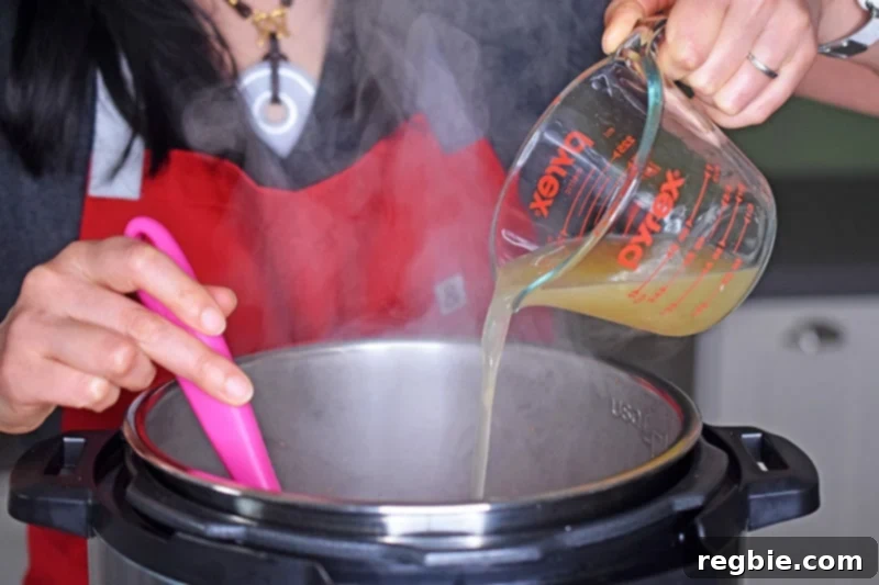 Pouring bone broth into an open Instant Pot, deglazing the pot to prepare for Orange Duck and gravy.